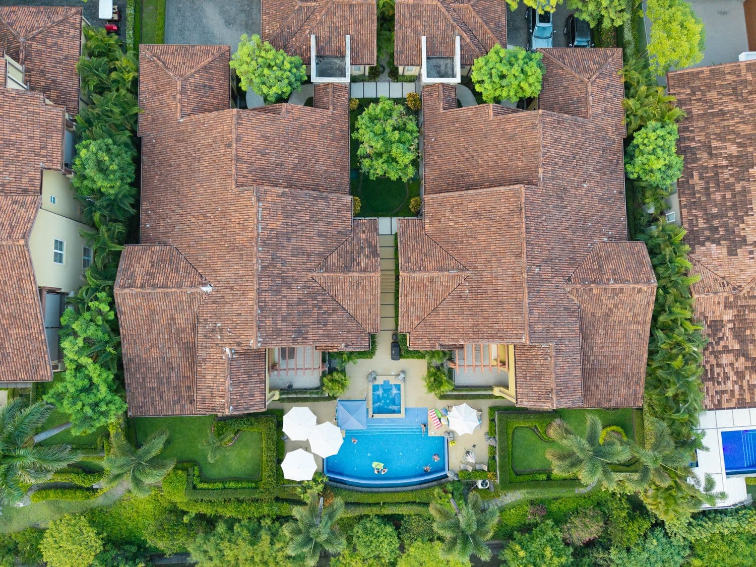 Aerial view of tile-roofed homes and a shared pool surrounded by tropical gardens