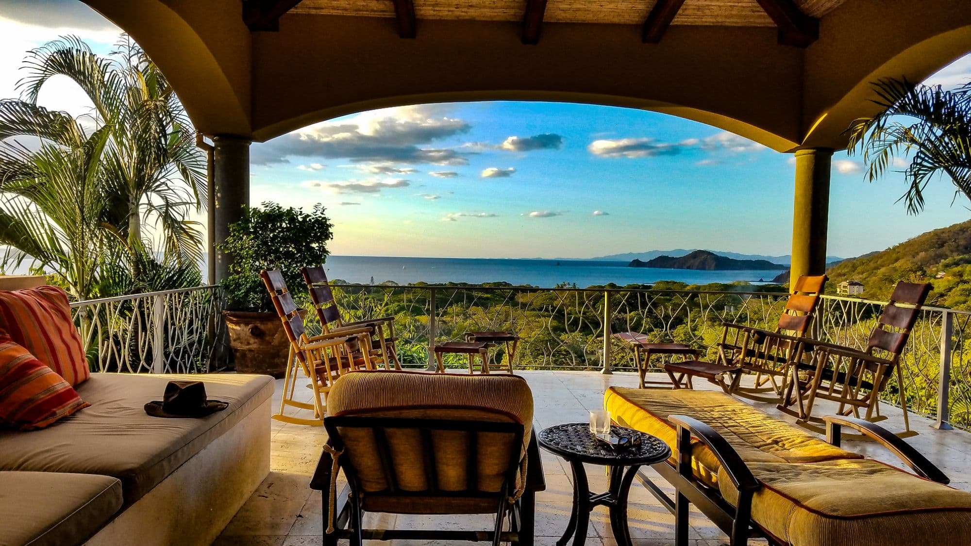 A covered terrace with rocking chairs looking out over a Costa Rica bay at sunset